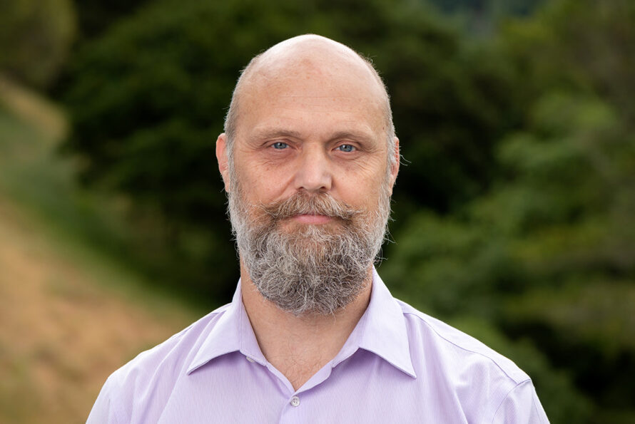 headshot of man wearing purple shirt against a green background