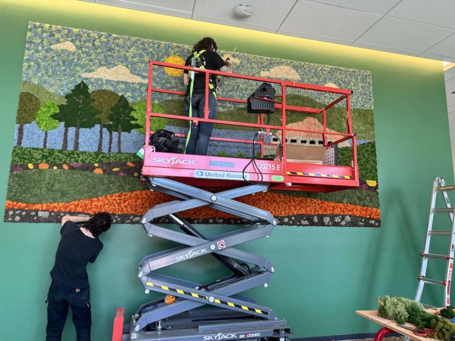 Person on a scissor lift and another standing on the floor installing the moss wall in the lobby of BioEPIC