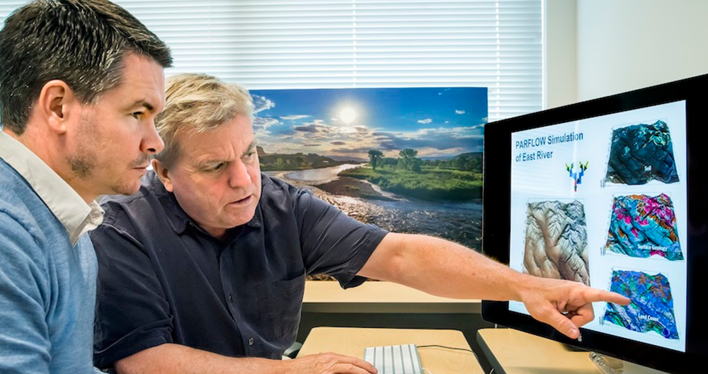 Photo of two scientists pointing at a computer screen with simulations of watersheds