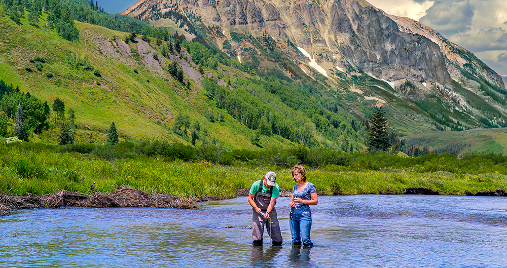Photo of scientists taking samples in a river overlooking crested butte, CO